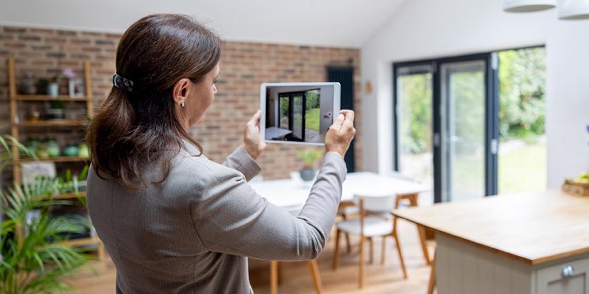 This image shows a person taking photos or a video of a home’s interior using a tablet. The individual is dressed in business attire, suggesting they may be a real estate agent or property manager capturing details for a listing or inspection. 